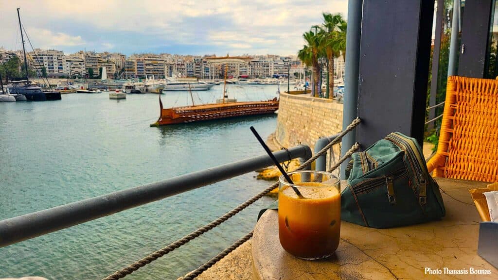 Iced coffee on a table overlooking a marina with boats and waterfront buildings