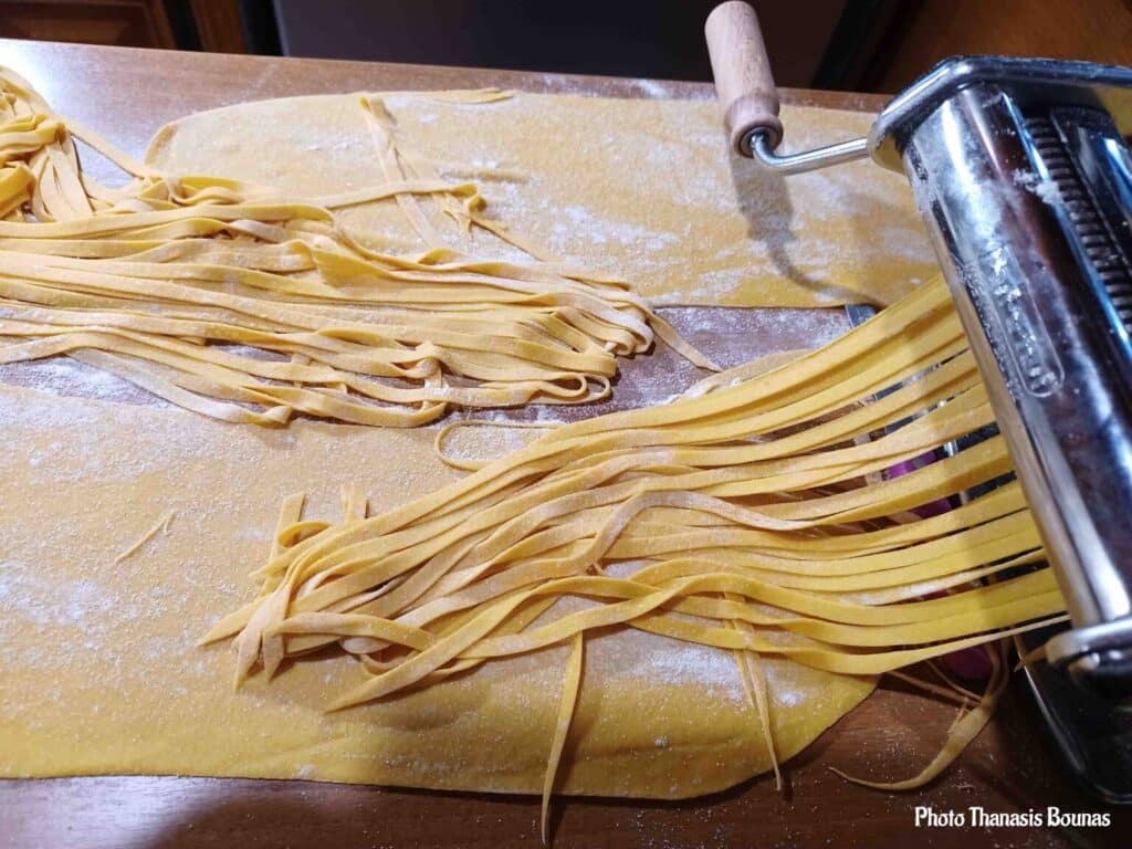Fresh pasta dough being cut into long noodles with a pasta machine