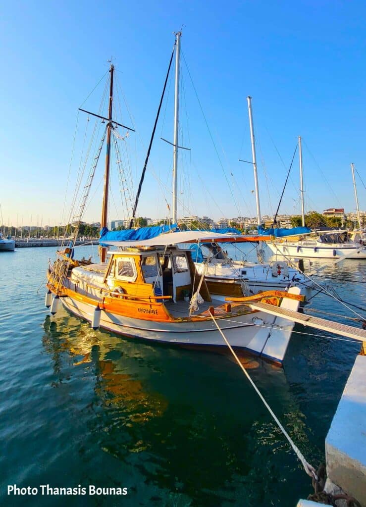 Traditional wooden fishing boat moored in a marina with sailboats and city buildings in the background
