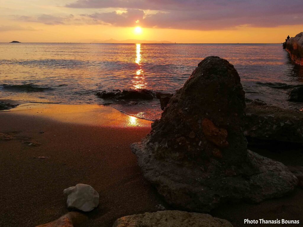 Sunset over a beach in Greece with rocks and golden reflections on the sea