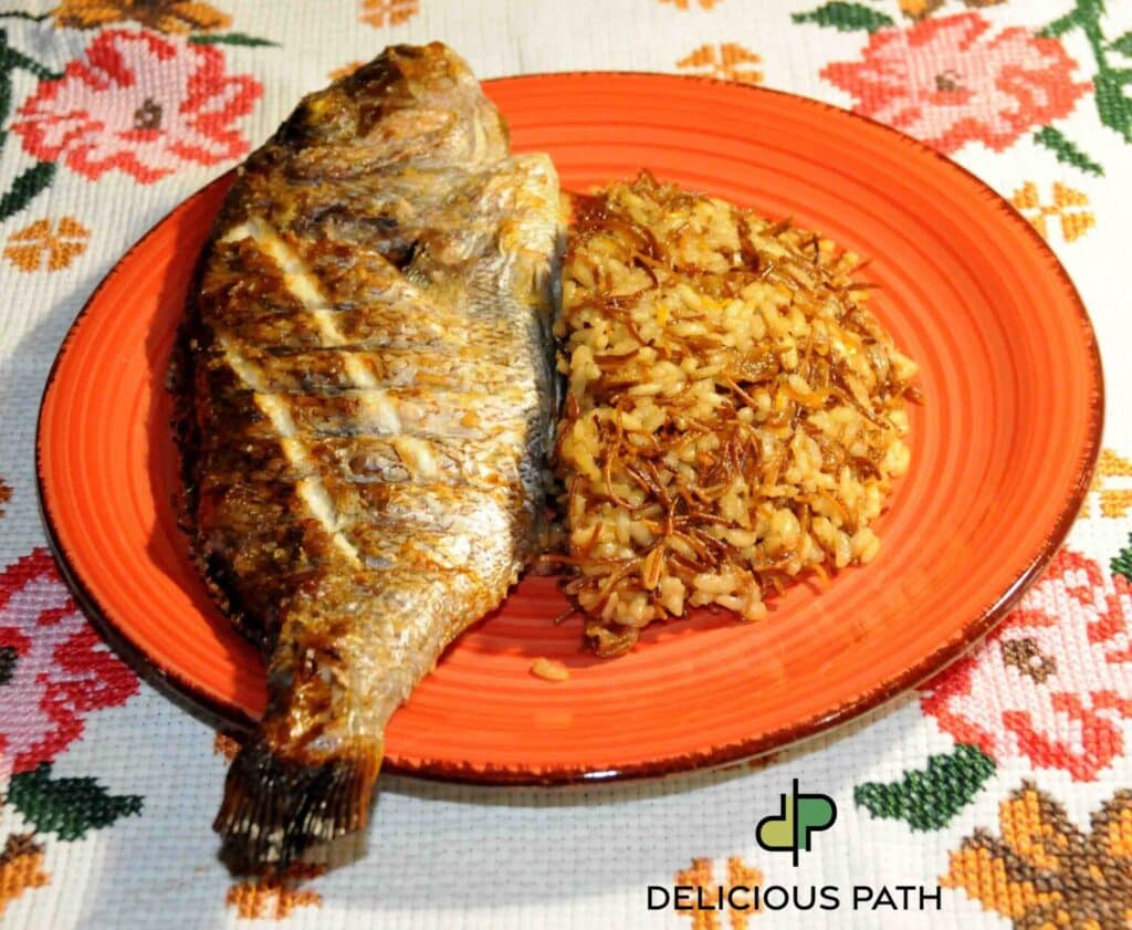 Grilled whole fish served with rice and toasted vermicelli on an orange plate