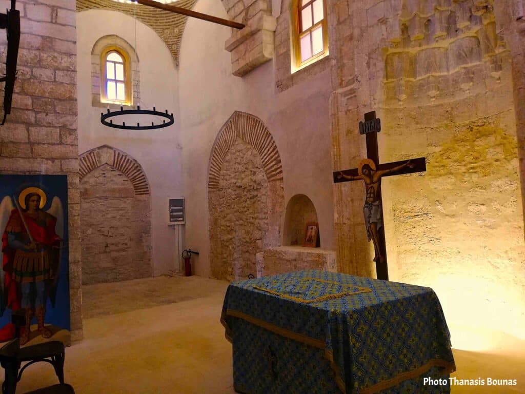 Interior of a historic Orthodox church in Greece with altar, cross, and stone walls