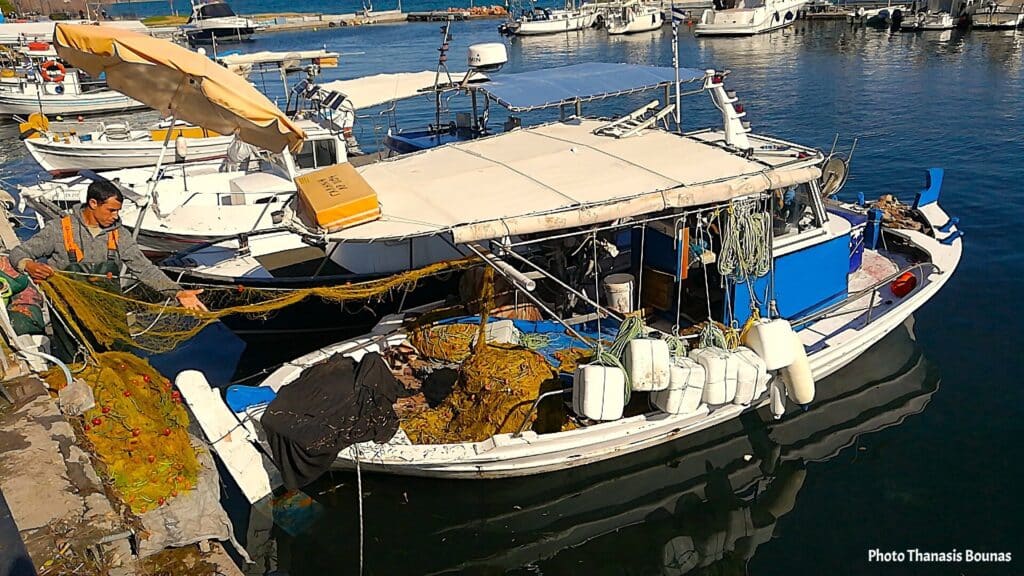 Fisherman arranging fishing nets beside a small traditional fishing boat at a harbor