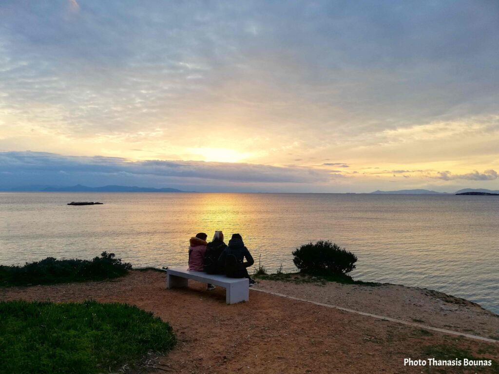People sitting on a bench watching sunset over the sea in Greece
