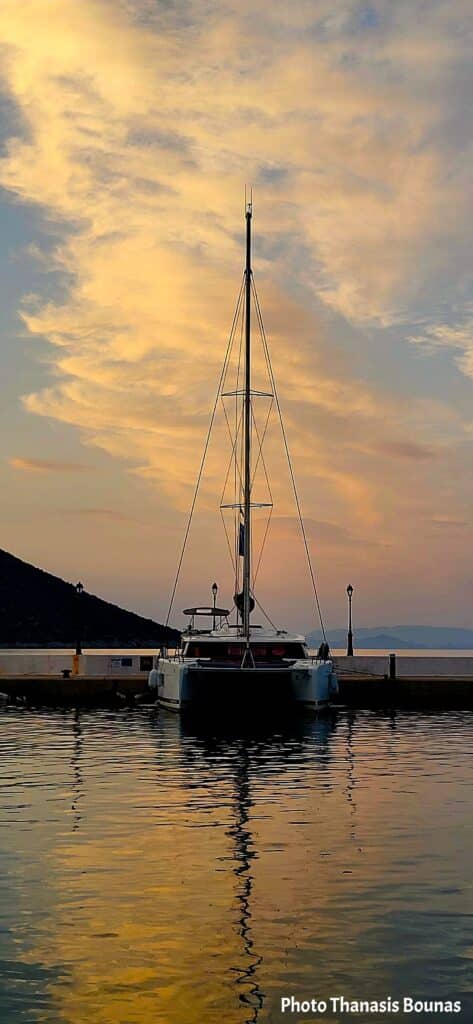 Catamaran sailboat moored at a quiet dock during sunset with golden clouds and reflections on calm water