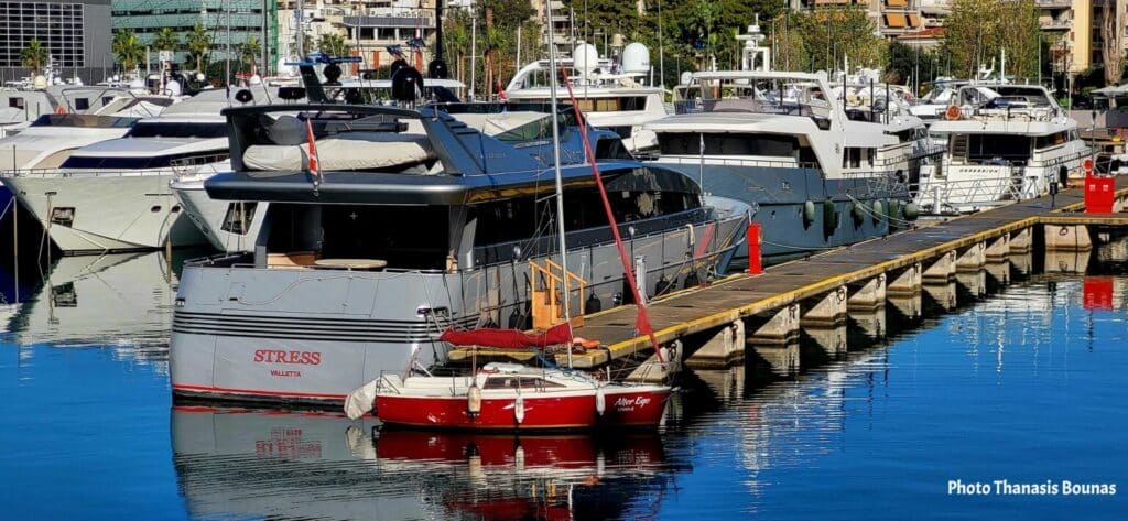 Luxury yachts and small sailboat docked at a marina with calm water reflections