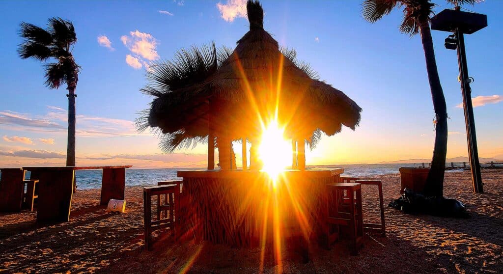 Beach bar on a Greek island at sunrise with sun shining through a wooden hut