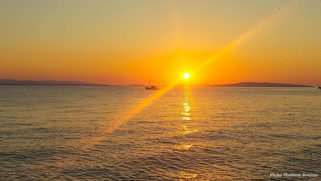 Sunrise at sea in Greece with small boat and golden reflections on the water