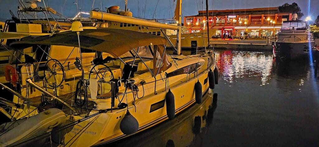 Sailboats moored in a marina at night with illuminated waterfront restaurant reflecting on the water