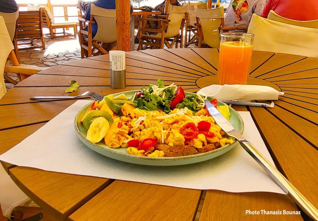 Plate of scrambled eggs with vegetables and fruit served on a wooden table at an outdoor café