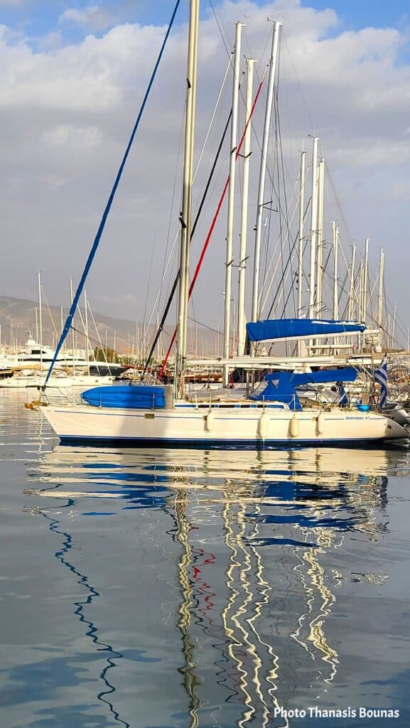 White sailboat with blue covers reflected in calm marina water, symbolizing balance, psychological equilibrium, and the philosophy of Sailing.