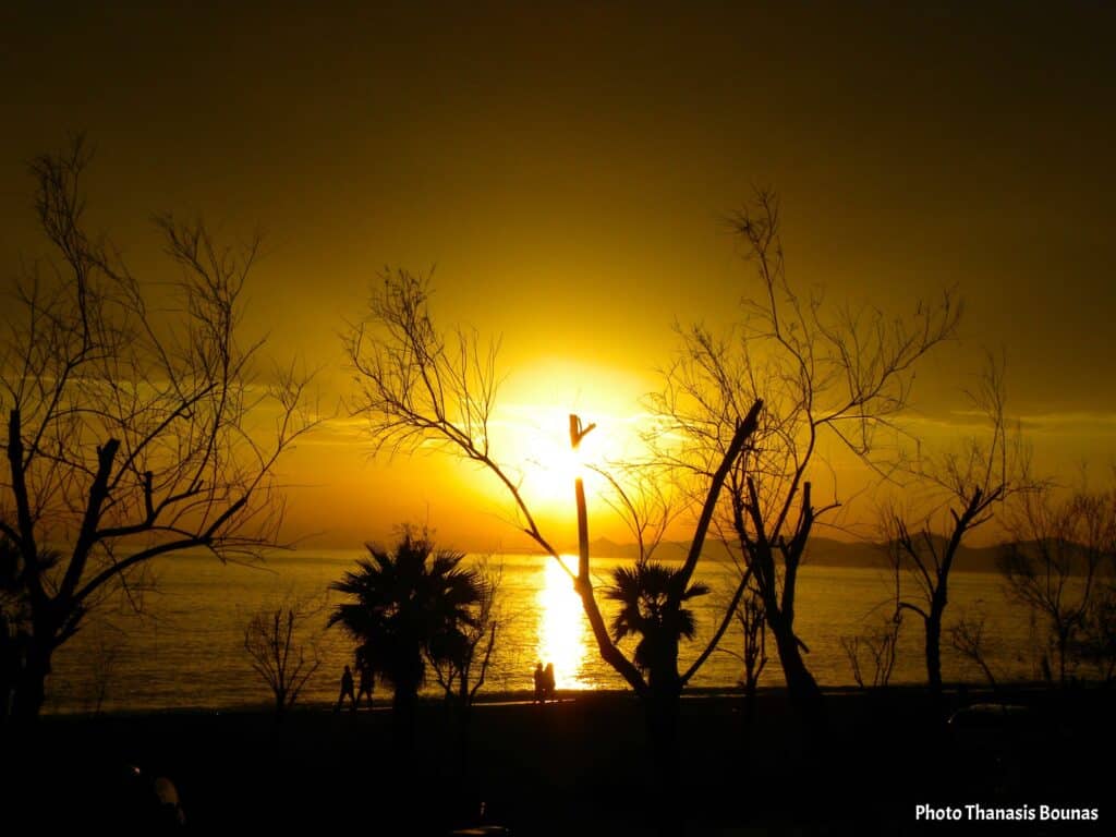Golden sunset at Kavouri Beach in Voula Greece with silhouettes of trees and people