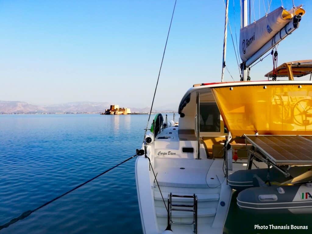 Sailing catamaran preparing for departure toward open sea with distant fortress on horizon