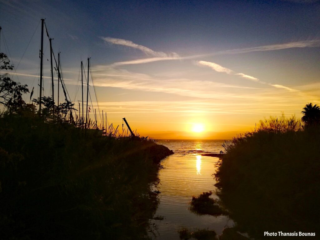 Sunset in Greece with sailing boat masts and calm water reflecting the light