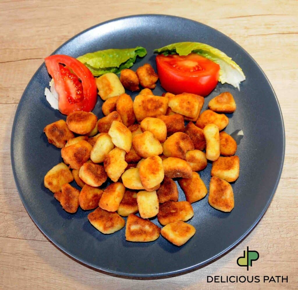 Dark plate with golden fried gnocchi and fresh tomato slices symbolizing hunger and psychological journey connected to sailing philosophy