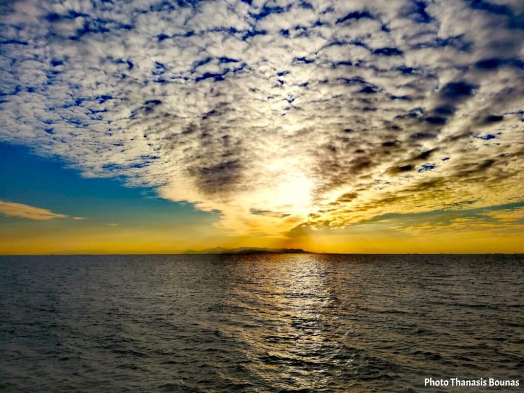 Sunset view from a sailboat in Greece with sea and distant islands under dramatic clouds