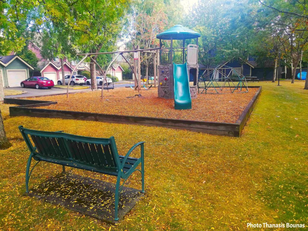 Quiet neighborhood park in Canada with bench and playground covered in autumn leaves