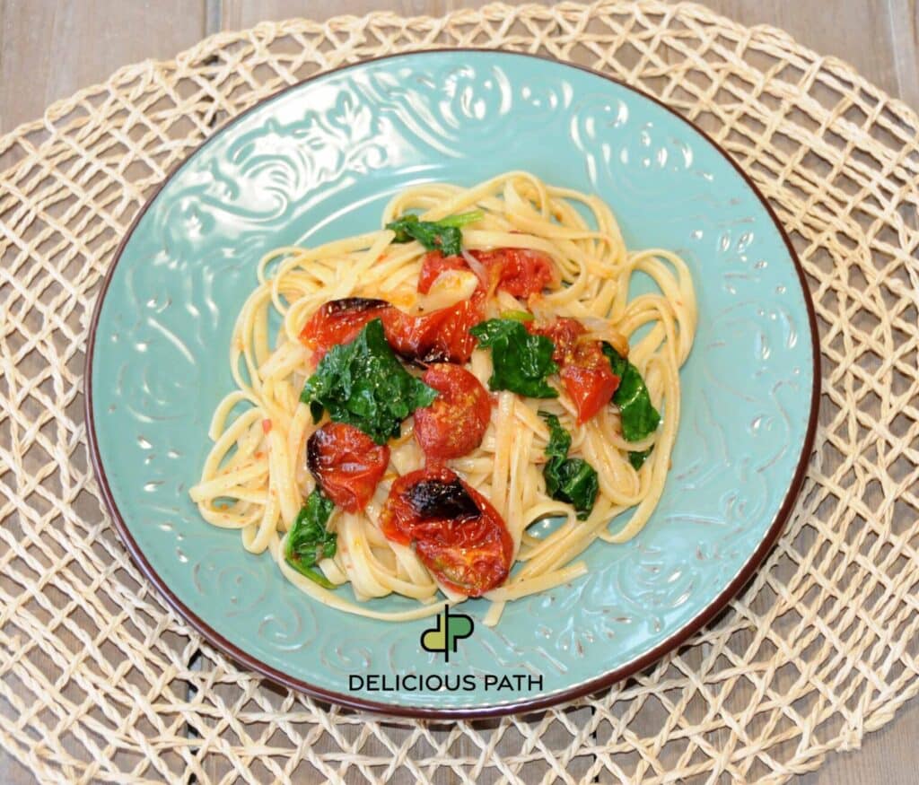 Plate of linguine with cherry tomatoes and spinach symbolizing promise, simplicity and sailing-inspired food philosophy.