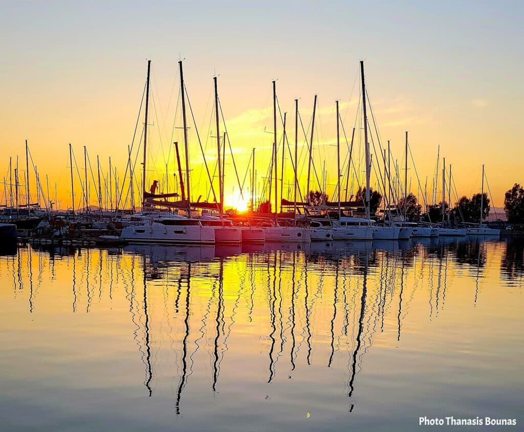 Sailboats at sunset reflected on calm marina water with golden light and still masts