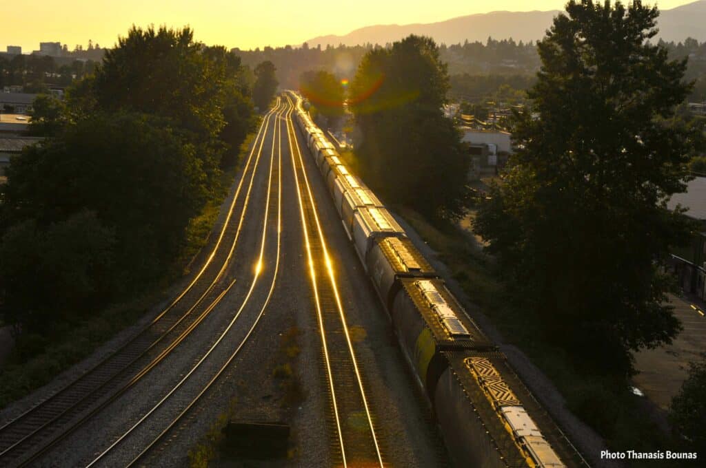 North Vancouver railway tracks at sunset with golden reflections leading toward Iron Workers Memorial Bridge