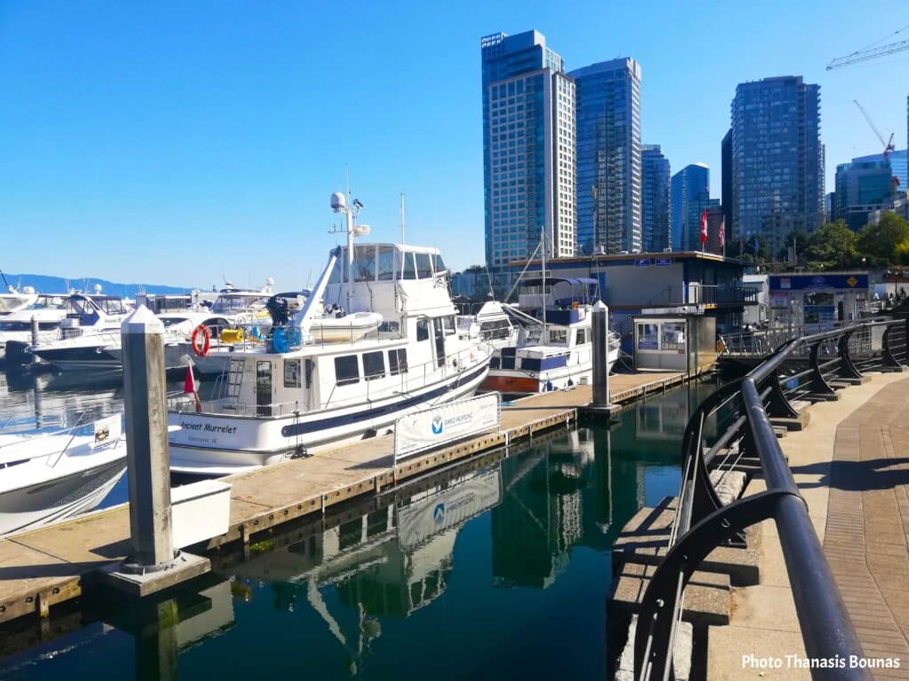 Boats docked at Vancouver marina with waterfront walkway and city skyline in Vancouver British Columbia Canada