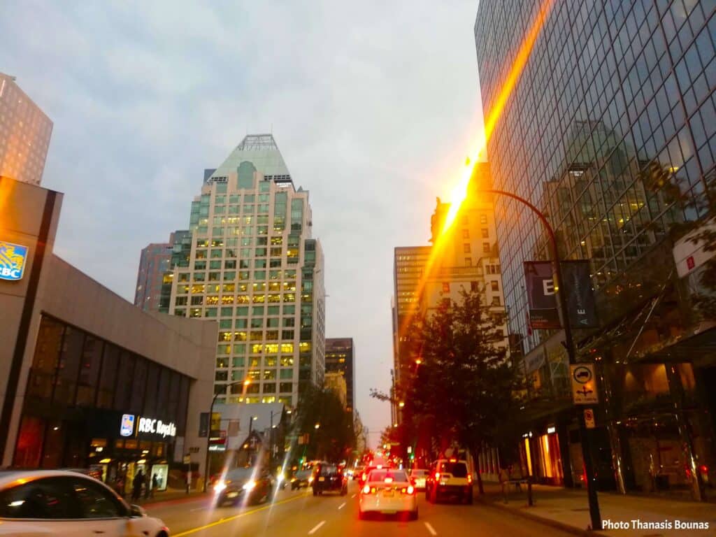 Downtown Vancouver street at sunset with city lights, traffic, and modern glass buildings