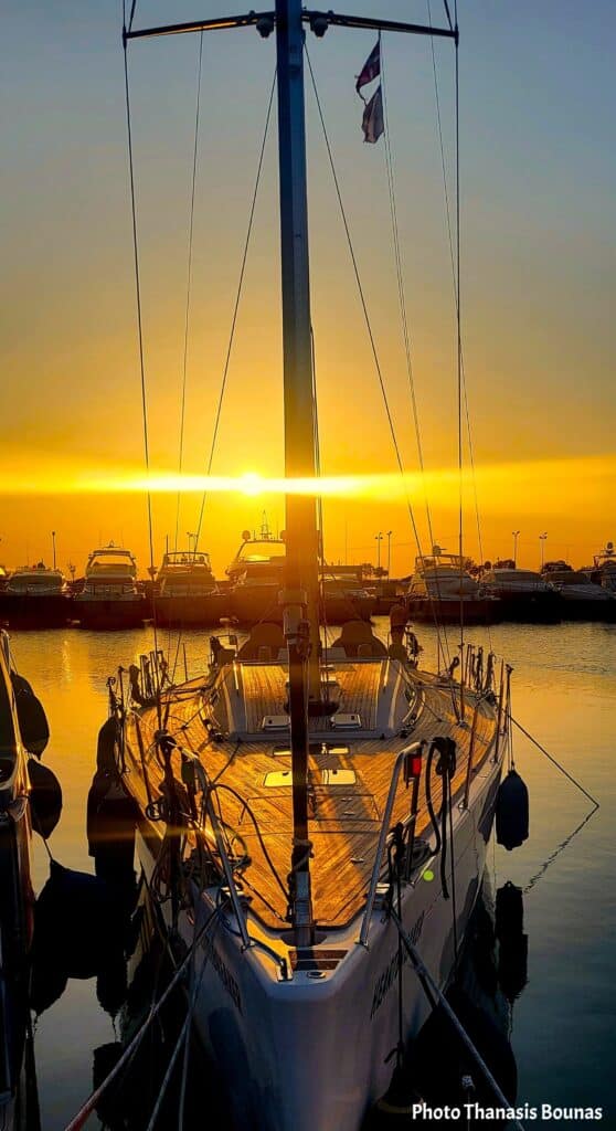 Sailboat docked in a marina at golden sunset with masts and yachts silhouetted against calm harbor water