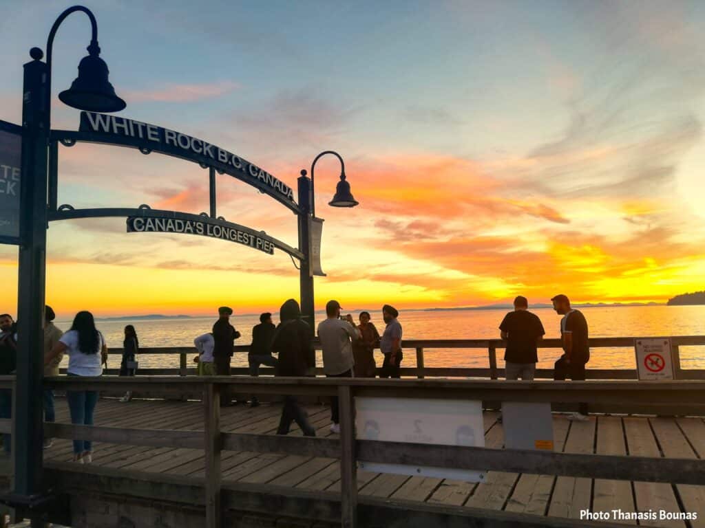 Sunset at White Rock Pier in British Columbia with people watching the horizon